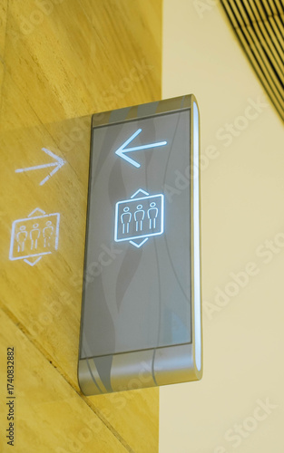 Elevator sign with three people on wall in a luxury shopping mall. Sign on the evelator wall with up and down arrows.