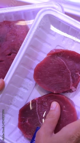 Customer hand touching and pressing a vacuum packed tray of fresh beef steak in a grocery store to check the quality and freshness of the raw red meat before buying it for dinner