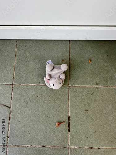 Small soft plush toy lying on green tiled floor near a door. Concept of childhood, forgotten items, lost belongings, or abandoned toys. Symbolic image for loneliness, nostalgia, or childhood memories