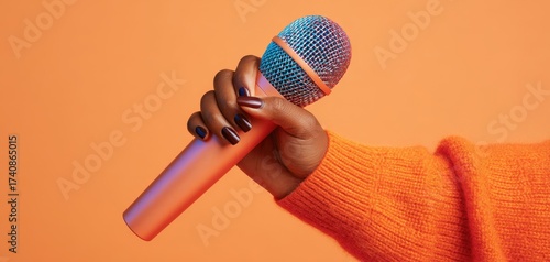 The microphone held in hand against vibrant orange background for singing performance