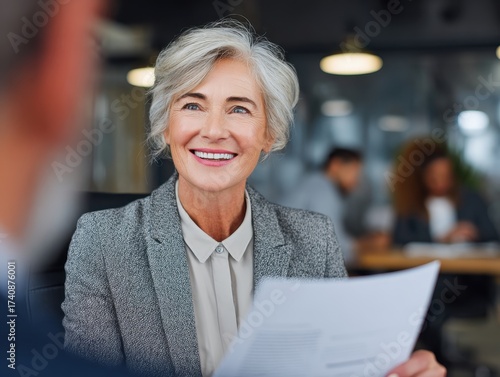 Smiling mature business woman hr holding cv document at job interview. Happy mid aged professional banking manager or lawyer consulting client sitting at workplace in corporate office meeting.