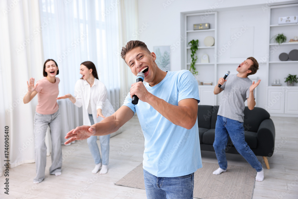 Obraz premium Young man singing karaoke with friends at home, selective focus