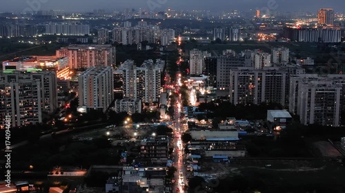 aerial drone shot passing over busy street filled with traffic between brightly lit skyscrapers extending off into the distance showing the bright cityscape of Gurgaon, Delhi, Mumbai