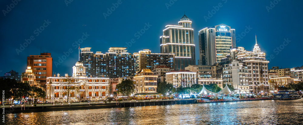 Obraz premium Guangzhou, Canton, China, 1 March 2025: illuminated colonial clock tower and historic riverside architecture at night. Modern skyscrapers and vibrant city lights reflected on the Pearl River.