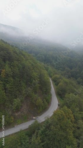 Aerial view of a winding mountain road surrounded by dense autumn forest covered with mist and fog	