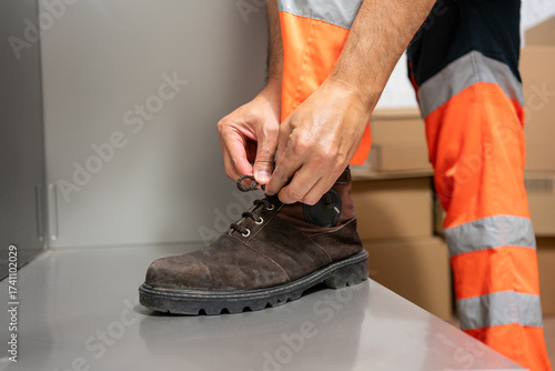 Close-up of a manufacturing worker's hands tying the laces on his work boots in a factory.