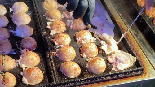A chef is grilling and rotating golden, crispy takoyaki balls, a beloved street food snack from Japan