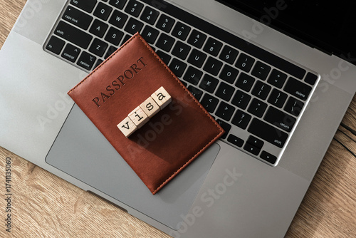 Brown passport holder with visa letter blocks on laptop keyboard, symbolizing international travel