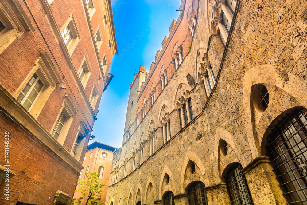 Obraz premium Photo of a narrow medieval street in Siena showing rustic stone facades, Tuscan details, charming alleys and authentic old town atmosphere in Tuscany Italy