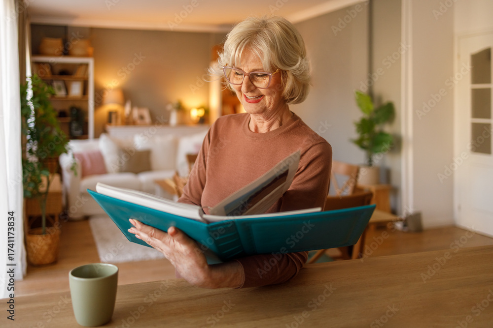 Εκτύπωση καμβά Elderly woman turning pages of photo album and cherishing family pictures while