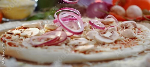 Vertical video of fresh red onion rings slowly falling onto a raw pizza base with tomato sauce, mozzarella cheese, and sliced mushrooms, representing the preparation of delicious homemade italian food