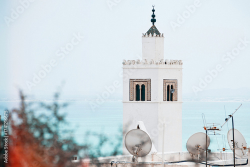 White islamic minaret tower of mosque of sidi bou said city against Mediterranean sea and sky on background - religious symbol. Tunisia