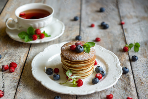 Delicate pancakes with fruits and berries on a wooden table.