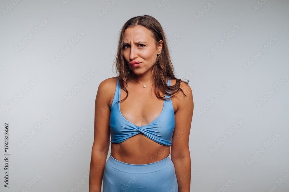 Fototapeta premium Woman in blue outfit makes a playful expression in a simple studio setting