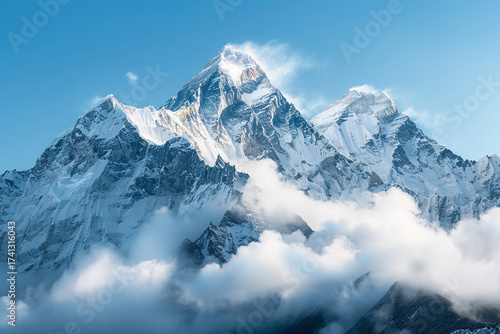 Majestic snow-capped mountain peaks pierce through soft clouds under a clear blue sky.