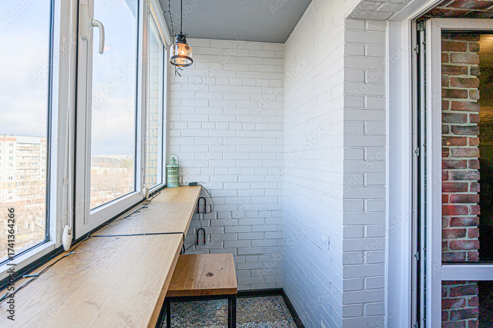 Fototapeta premium A cozy balcony with white brick walls, a wooden countertop by the window, and a hanging light