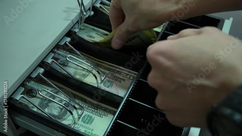 The man opens the cash register with dollars. The cashier puts the dollar money in the cash register and takes the change. Retail for cash DOLLARS