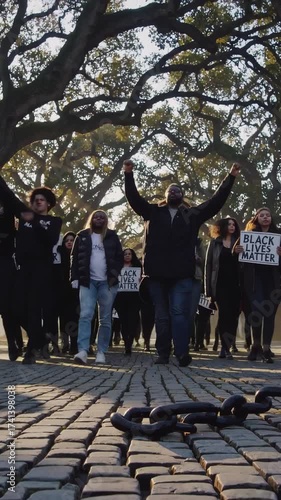 Black people raising their arms in triumph and awareness, participating in a social justice protest for equality and freedom, with broken chains lying on the cobblestone street