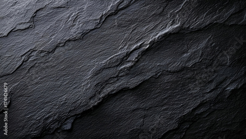 Textured dark slate stone surface with natural patterns and shadows, ideal for backgrounds and design projects.