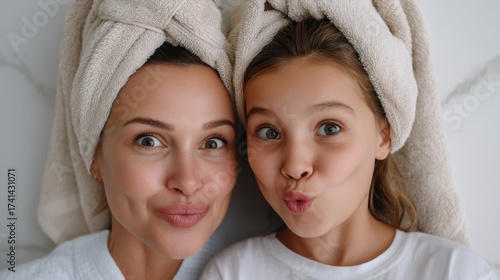 Top angle shot of playful mother and little daughter during morning skincare routine, towels on heads. 