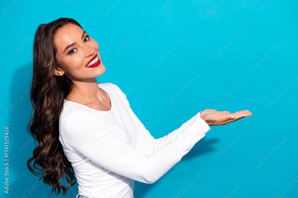 Fototapeta premium Cheerful young woman in white presenting or promoting with a vibrant smile against a vivid blue background
