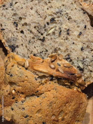 Obraz na plátně Slices of freshly baked multigrain bread with a crunchy crust, densely packed with sunflower, chia, and pumpkin seeds on a wooden surface