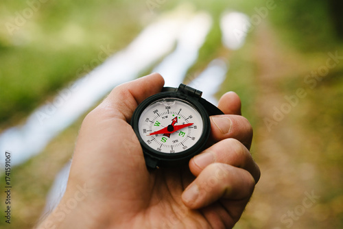 A compass in a man's hand on a green forest background.