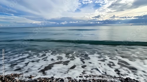 Ocean waves with white foam gently lapping onto a sandy shore under a dramatic cloudy sky with sunlight breaking through
