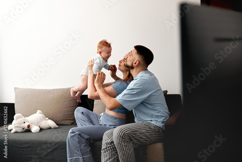Joyful family moment with parents playing and bonding with their baby on a cozy couch in a modern living room, family love concept