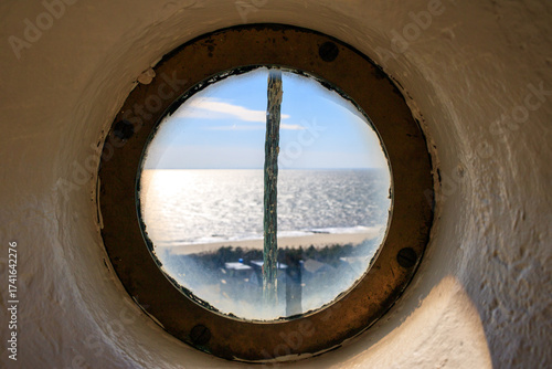 View of the ocean through a round window from a lighthouse on a sunny day by the coast