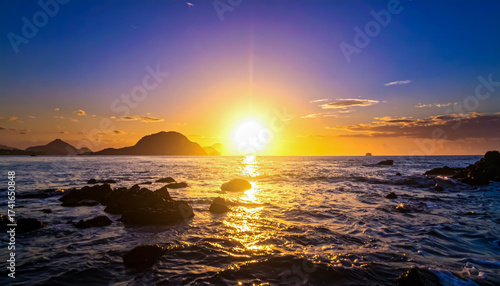 Sunrise or Sunset over the Ocean with Mountain Silhouettes and a Rocky Shoreline