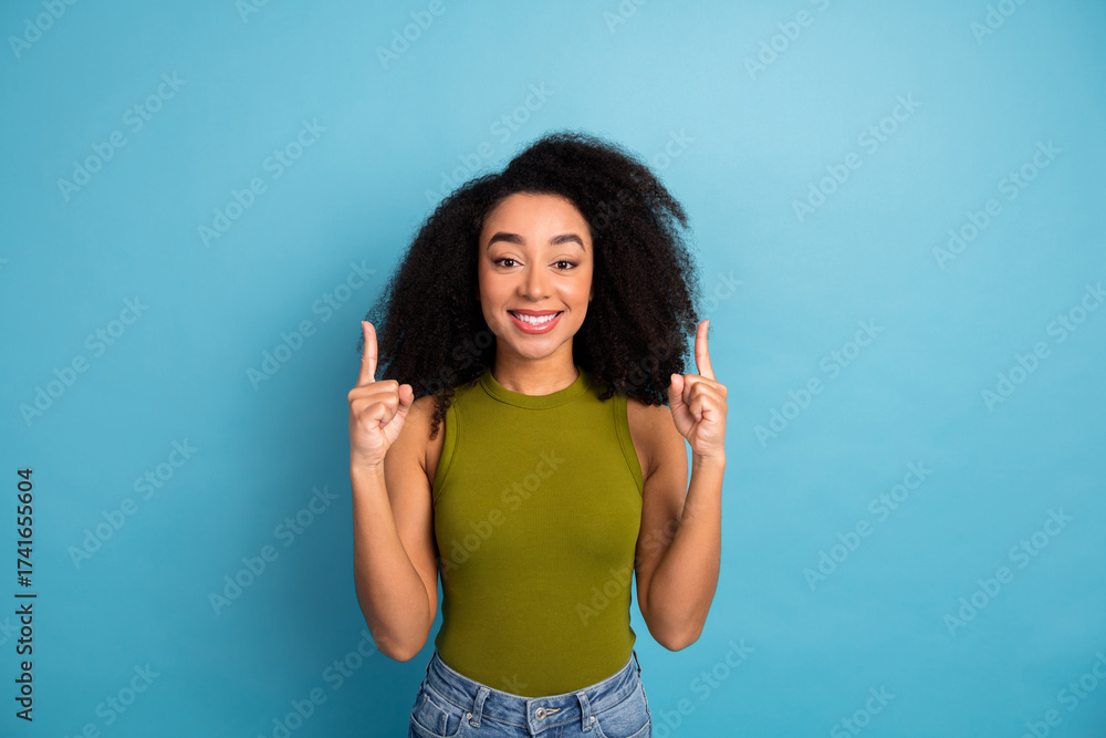 Fototapeta premium Smiling young woman in a green top making pointing gestures against a vibrant blue background