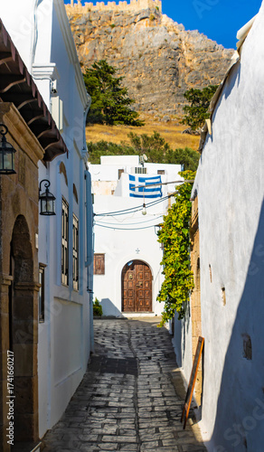 Beautiful narrow alley with whitewashed walls, Acropolis in the background, Lindos, Rhodes, Greece