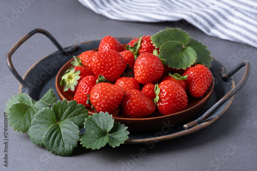 Freshly picked strawberries arranged neatly on a brown wooden plate with green leaves nearby