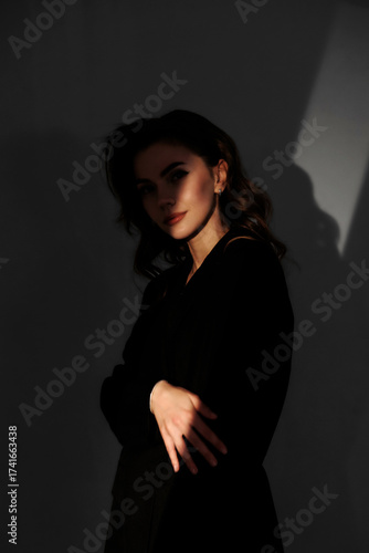 Soft light creates mysterious shadows around a woman in a dark outfit in a minimalist room