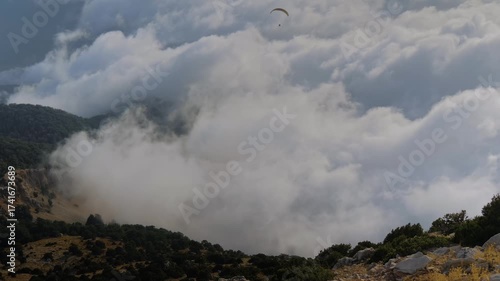 Time lapse: fast drifting white clouds hover below the summit of Babadag mountain, with occasional paraglider gliding by. Adventure, timelapse, nature, and aerial perspective concept