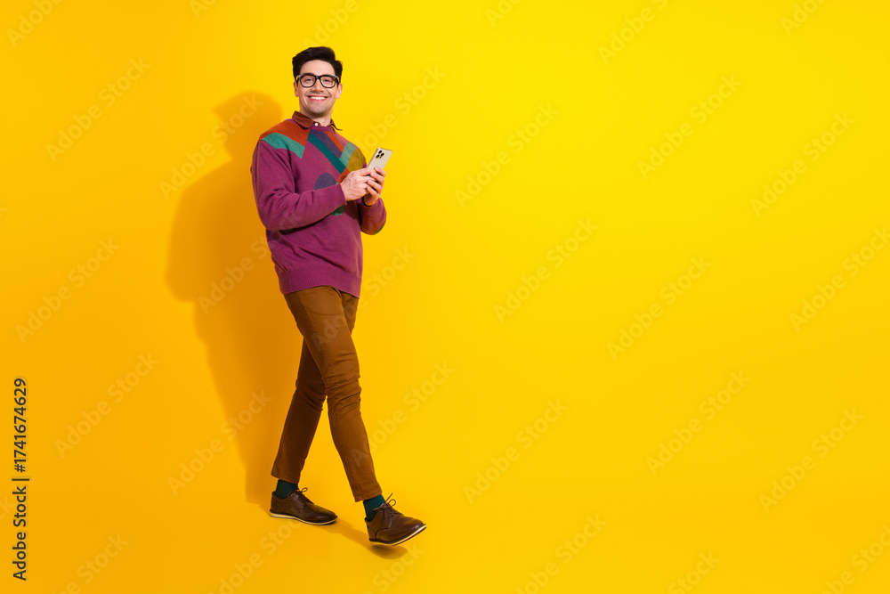 Fototapeta premium Confident young man in retro sweater using a smartphone against a vibrant yellow background