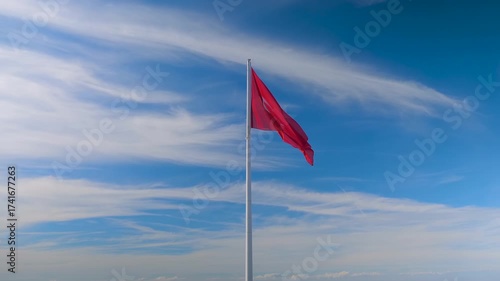 The red national flag of the Republic of Turkey is fluttering in the wind on Mount Babadag against the blue sky with white clouds. Symbol of national unity, diplomacy, and heritage