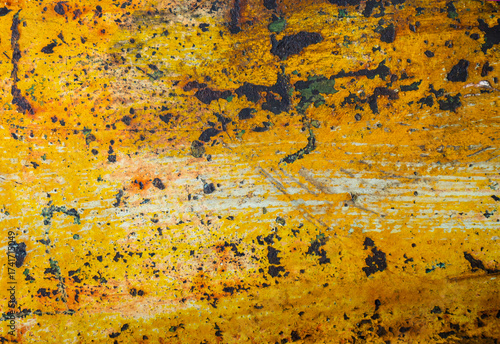 An abstract grunge texture background of an old metal surface. Faded and peeling yellow paint reveals the rust and scratches underneath, creating a worn, industrial pattern.