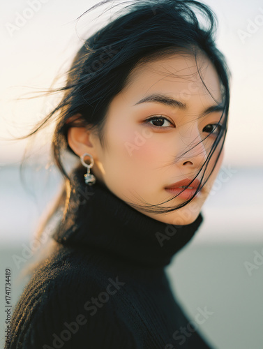 A photograph of an asian woman with dark hair, wearing earrings and a black turtleneck sweater, in a close-up frontal view