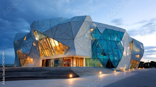 Geometric architectural  illuminated at dusk, showcasing a modern building facade with triangular glass panels and a dramatic cloudy sky backdrop, revealing warm interior light from within the...