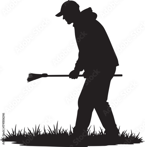 Silhouette of person in baseball cap sweeping grass