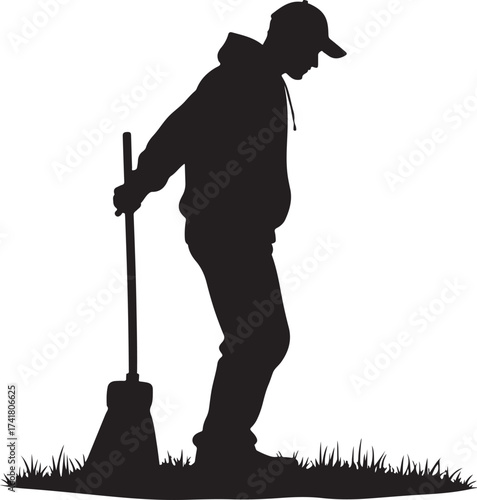 Silhouette of person in hoodie and cap holding broom on grass