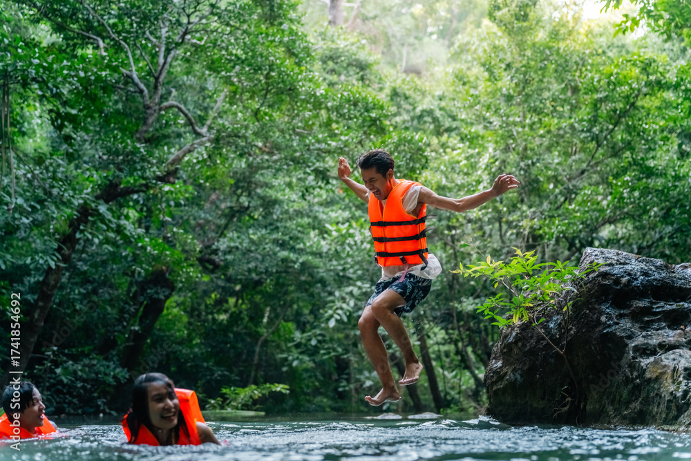 Obraz premium Young Asian man and woman travel nature forest hiking and camping on summer holiday vacation. Generation z people friends enjoy and fun active lifestyle playing water in waterfall lagoon in sunny day.