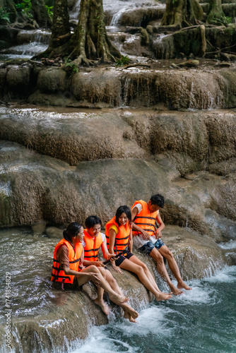 Young Asian man and woman travel nature forest hiking and camping on summer holiday vacation. Generation z people friends enjoy and fun active lifestyle playing water in waterfall lagoon in sunny day.