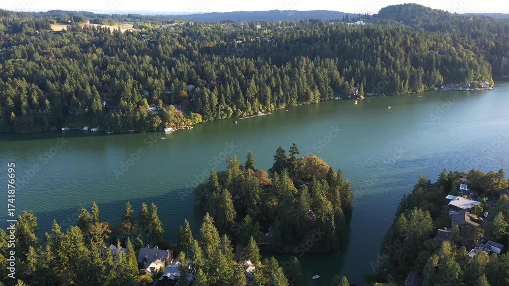 4K aerial drone footage of Lake Oswego, Oregon, showing calm blue water surrounded by dense forest and residential homes on a clear sunny evening. Captured during earl fall season from high altitude.
