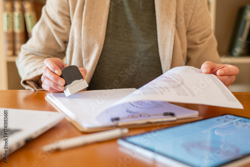 Person's hands holding a rubber stamp, making an official mark on a paper document on a clipboard, signifying approval and agreement in legal, banking, and real estate finance