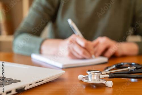 Medical student training for future healthcare by studying and writing notes at a desk with a laptop and stethoscope, highlighting dedication to clinical knowledge and professional development