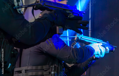 Special police unit officers during a weapon demonstration, dressed in black tactical uniforms, illuminated by blue stage light during a public police presentation