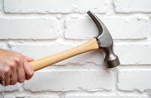 Hand holds hammer ready to hit white brick wall. Concept for destruction anger frustration or construction problem solving and home repair idea.